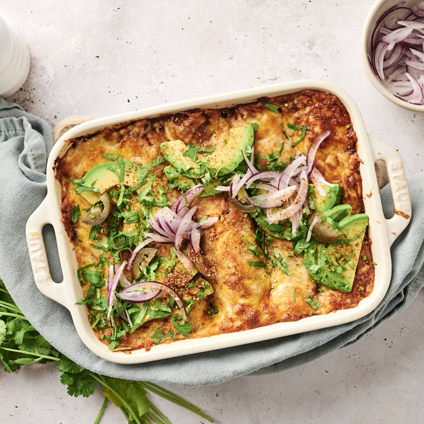 Easy Chicken Enchiladas A close-up of cheesy chicken enchiladas being served from a casserole dish, topped with avocado, red onion, jalapeños, and fresh cilantro.
