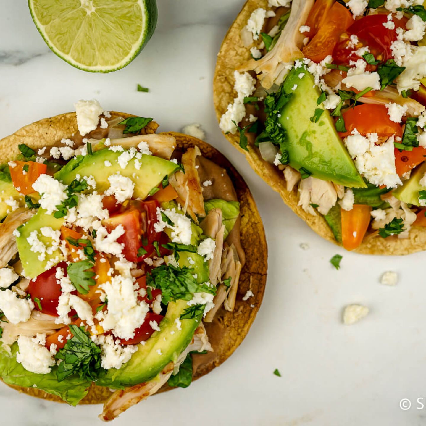 Chicken tostadas with refried beans, chicken, lettuce, salsa, cheese, and cilantro.