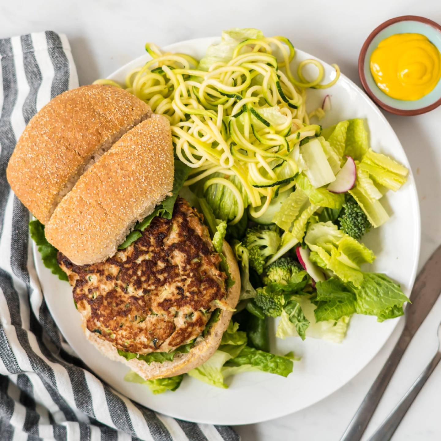 Chicken zucchini burgers on a plate with fresh herbs and ricotta cheese.