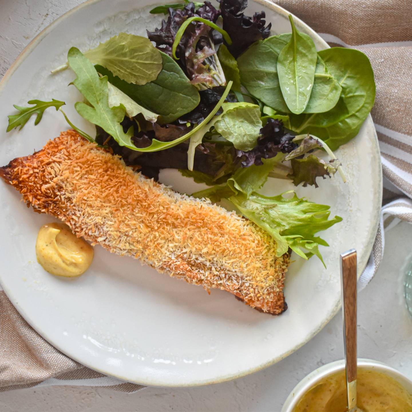 Coconut crusted salmon coated with crispy shredded coconut and spices on a plate with a mixed green salad.