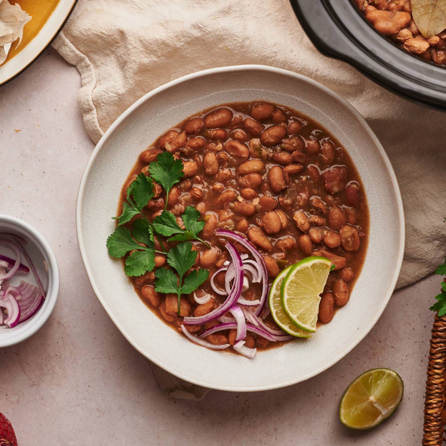 Crockpot pinto beans in a bowl with red onions, cilantro, and lime slices. 