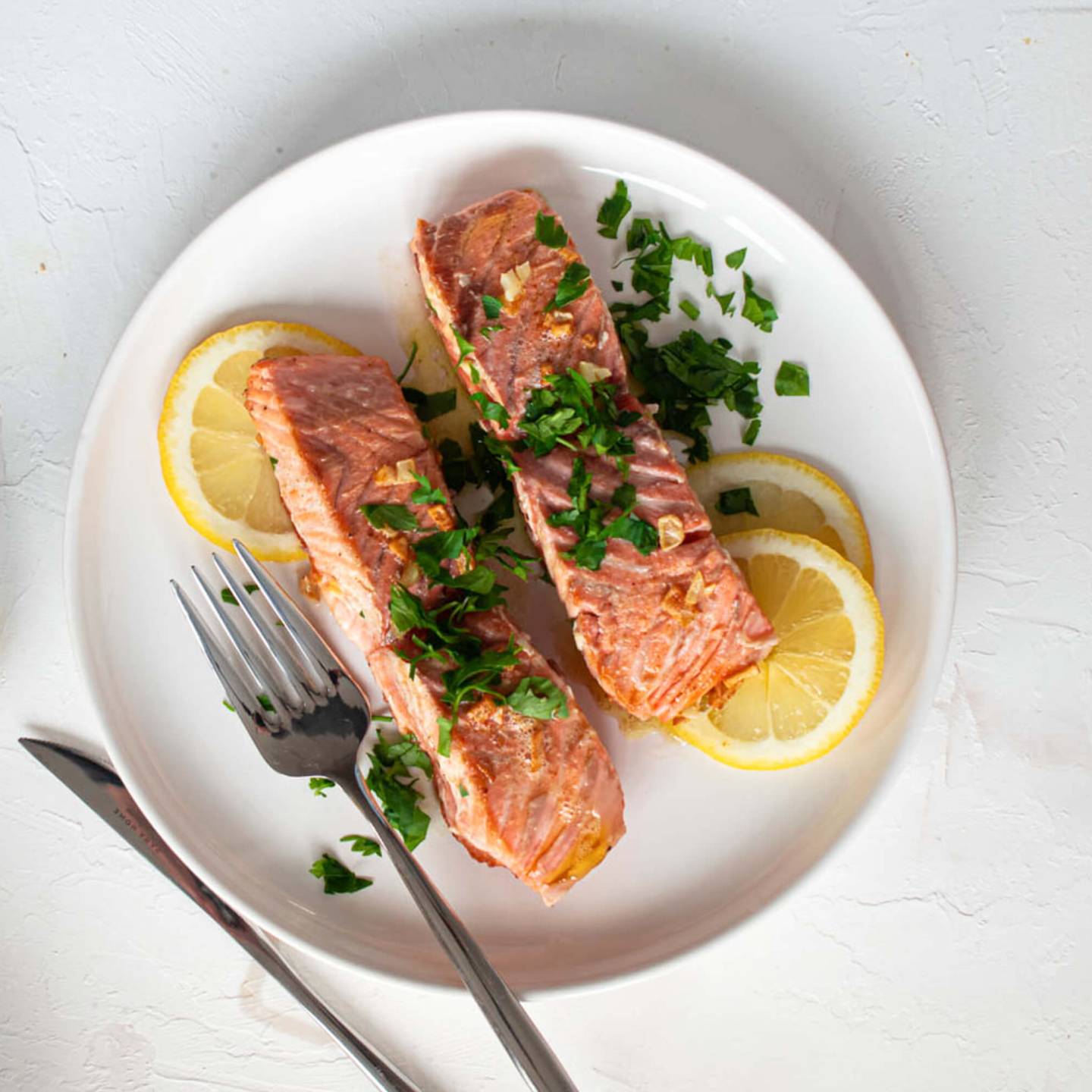 Dijon baked salmon with a garlic, lemon, and Dijon mustard sauce on a plate with garlic on the side.