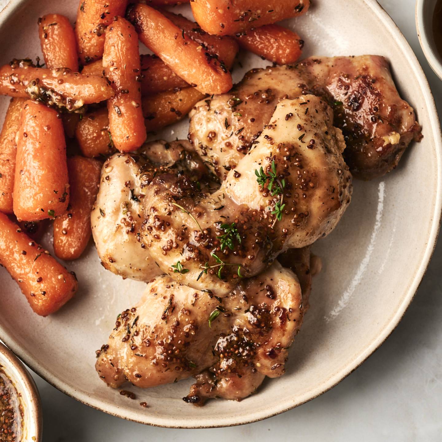 A plate features succulent chicken thighs glazed with mustard and herbs, accompanied by roasted, seasoned carrots.
