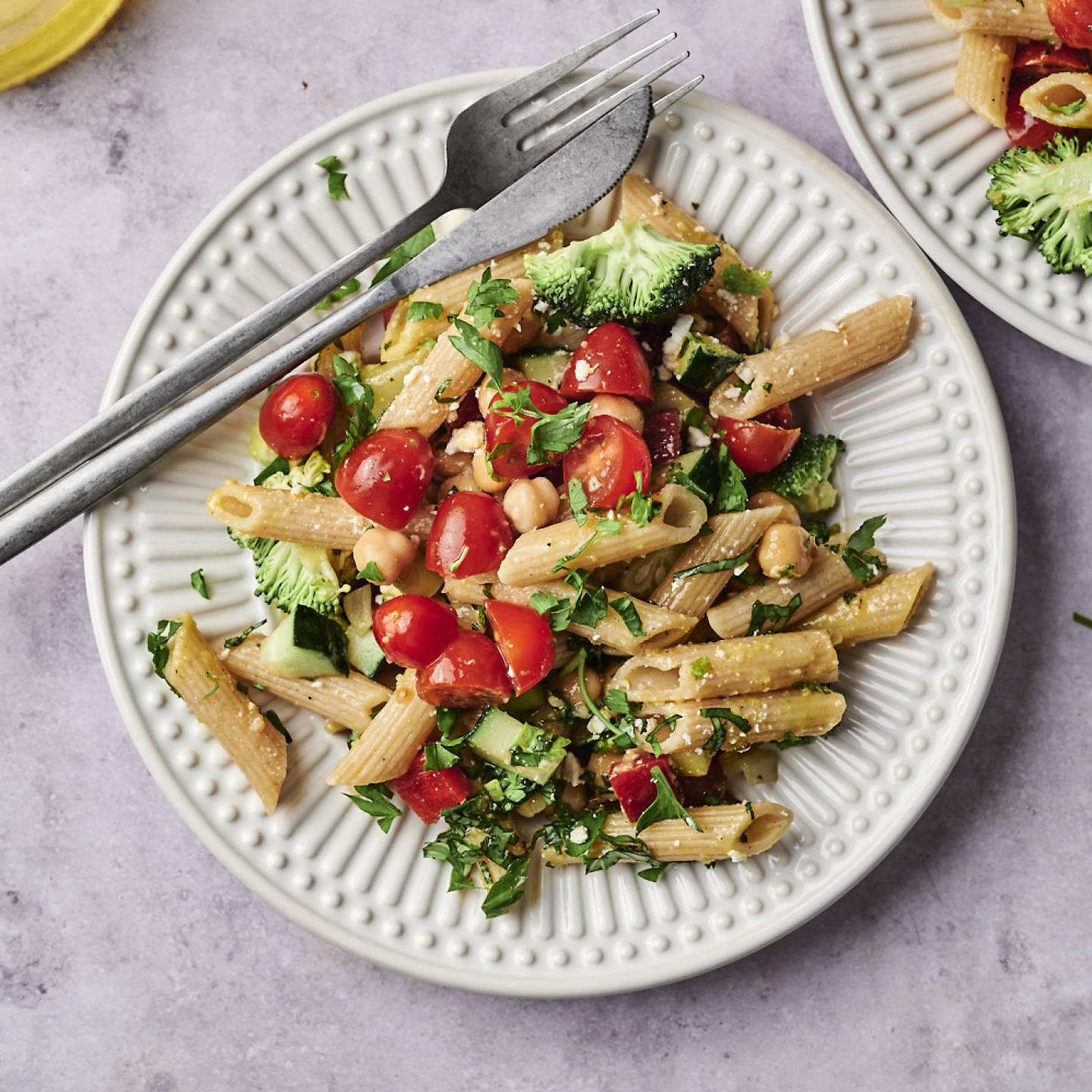 Easy Vegetable Pasta Salad A vibrant plate of pasta mixed with cherry tomatoes, broccoli, and herbs, accompanied by a glass of olive oil and fresh basil leaves.