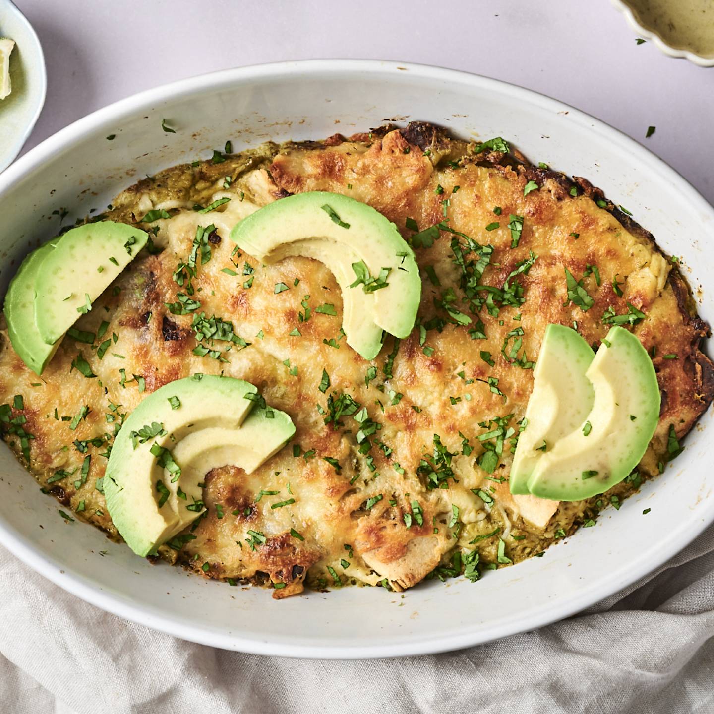 A freshly baked dish of enchiladas topped with avocado slices, sour cream, cilantro, and seasoning.