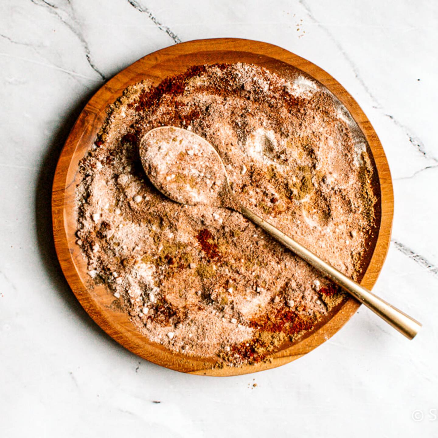 Fajita seasoning with chili powder, paprika, garlic powder, onion powder, and cumin mixed on a wooden plate.
