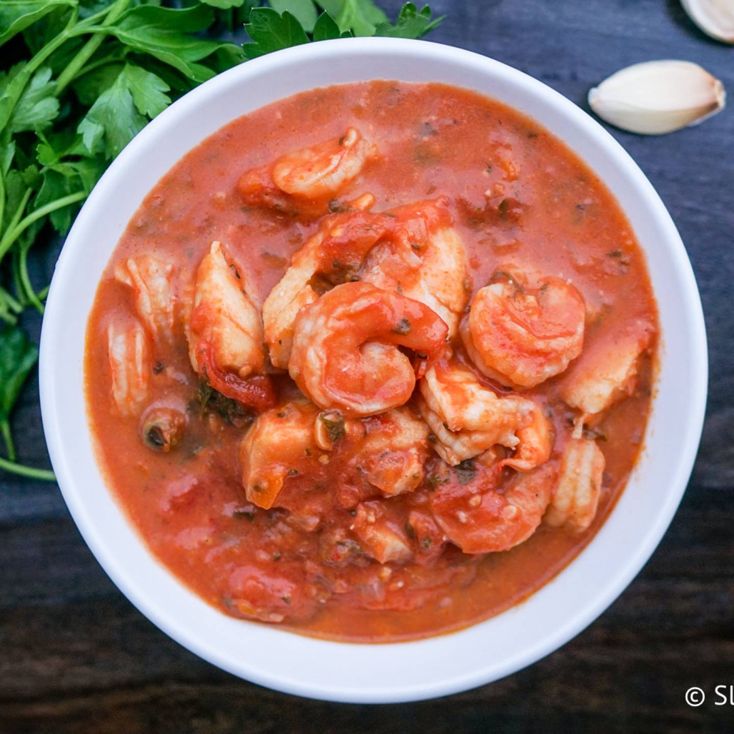 Fish and shrimp stew in a bowl with a tomato and garlic broth.