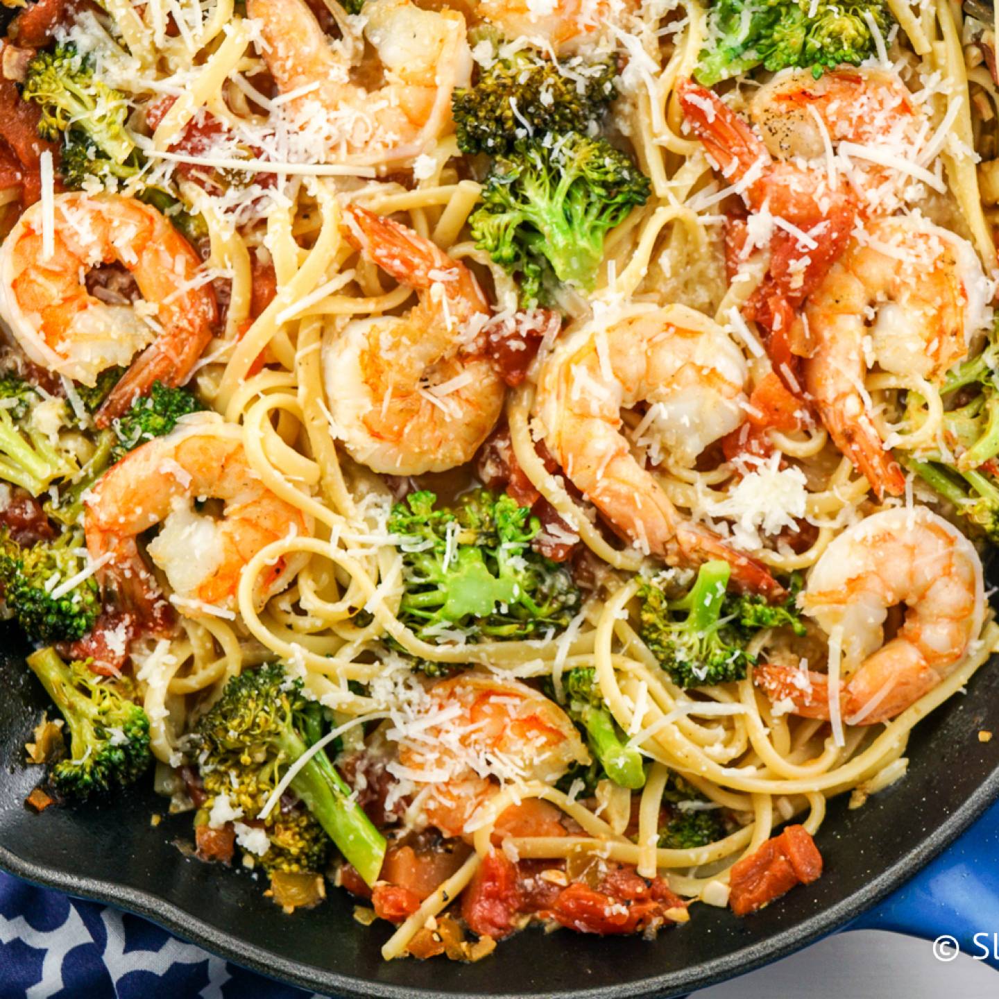 Garlic lemon and shrimp and broccoli pasta in a pan with fresh lemon slices and Parmesan cheese.