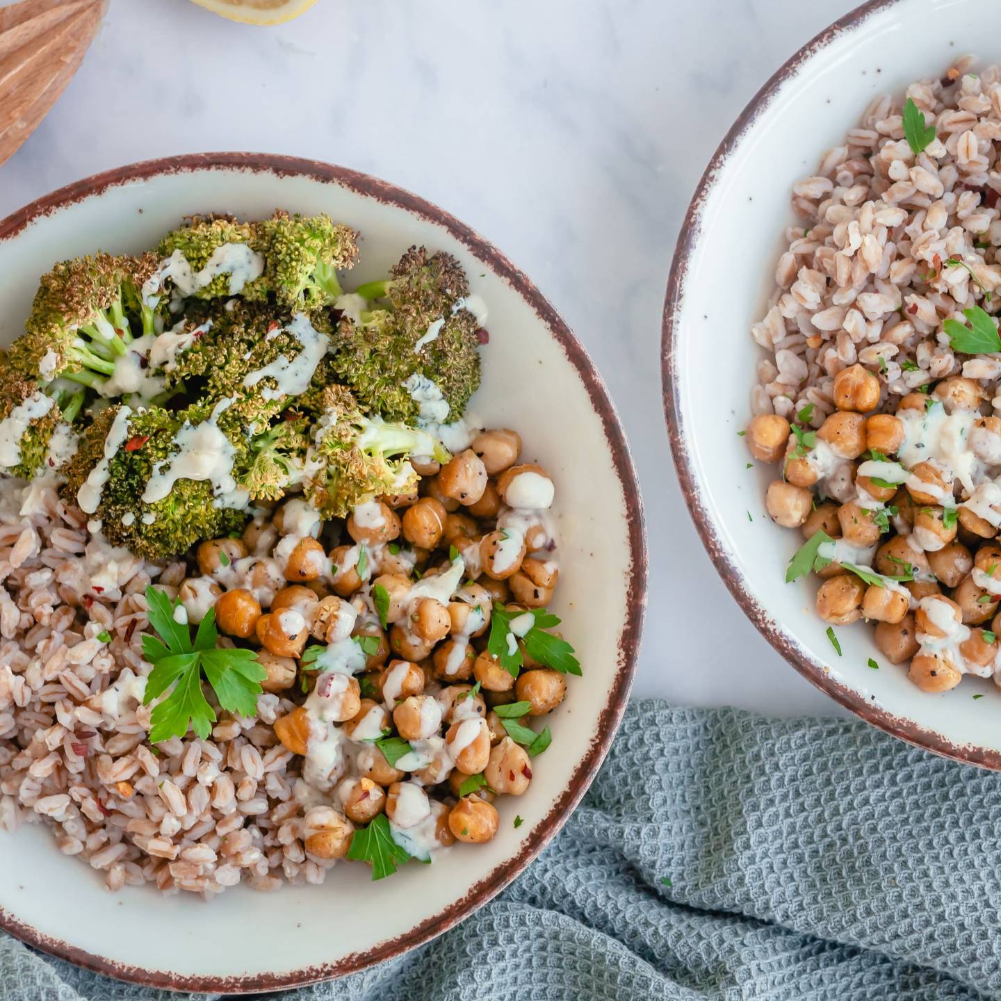 Garlic tahini broccoli bowls with cooked farro, roasted broccoli, roasted chickpeas, and tahini sauce in two bowls.