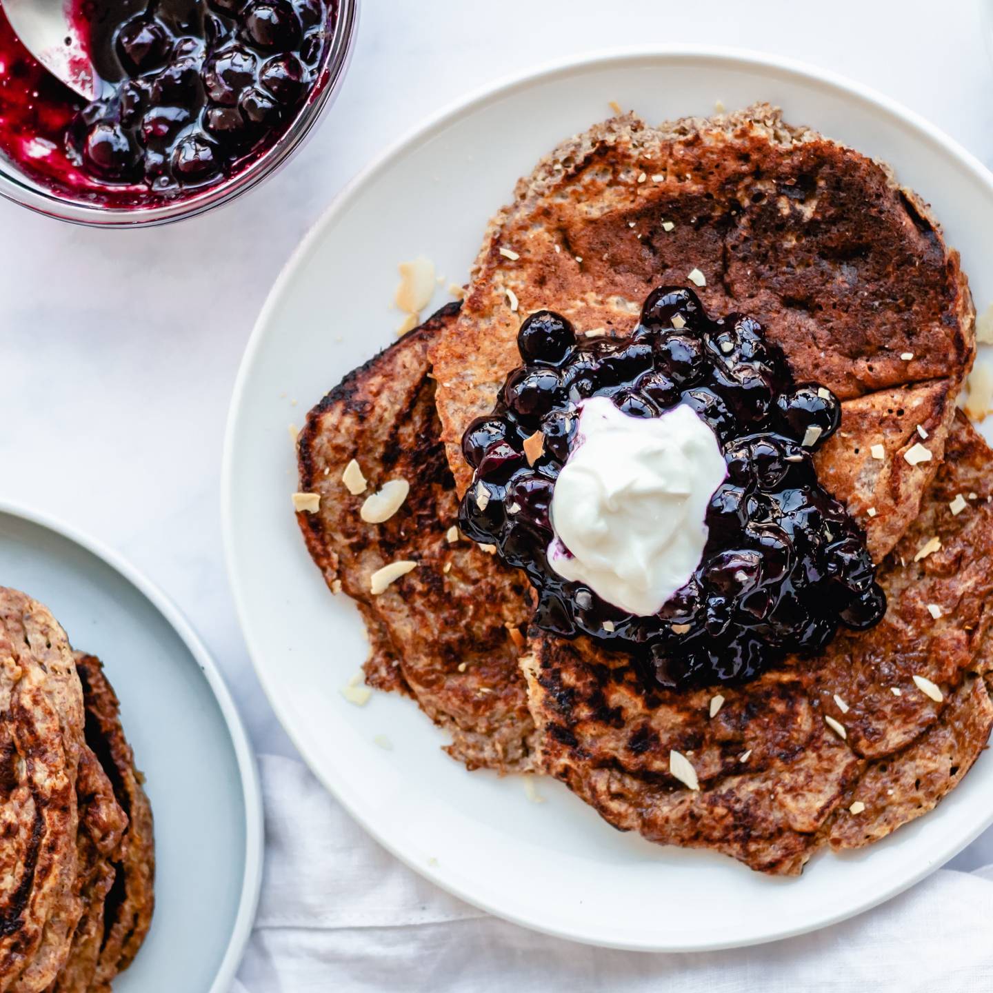 Greek yogurt and flax pancakes on a plate with blueberry compote, whipped cream, and almonds.