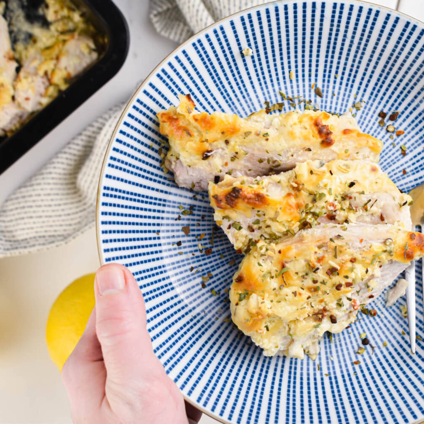 Baked Greek Yogurt Parmesan Chicken with herbs, lemon juice, Parmesan cheese, and garlic on a blue plate.