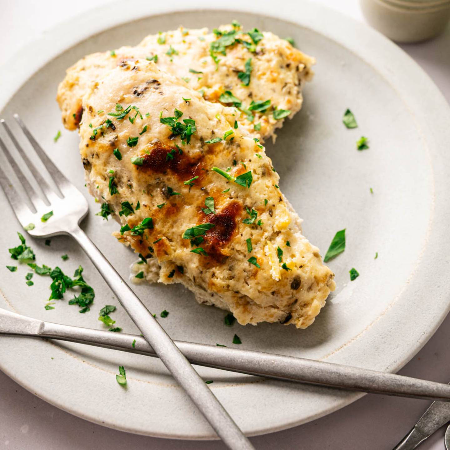 Creamy baked Parmesan chicken breasts in a casserole dish, garnished with chopped parsley.