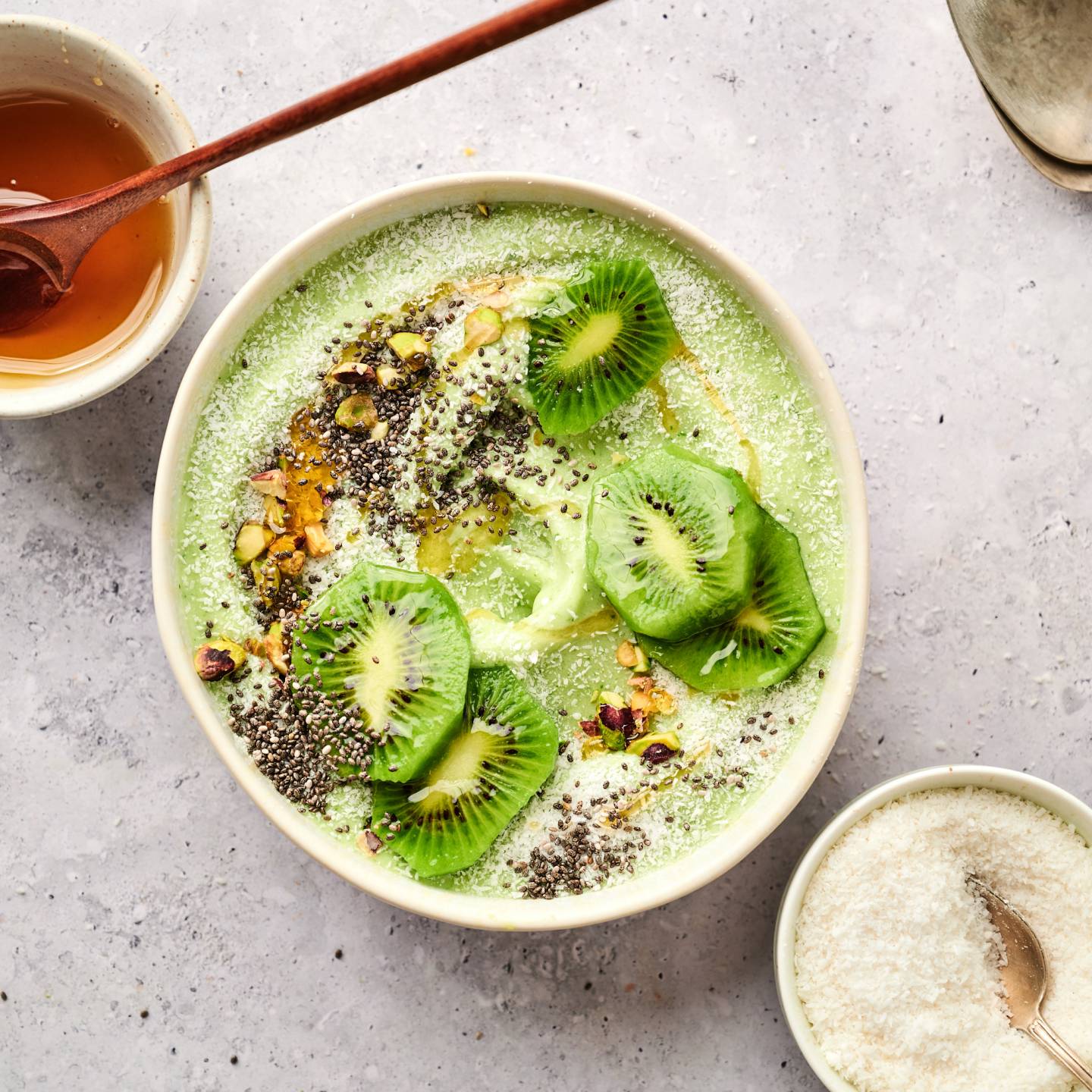 Green smoothie bowl made with banana, mango, pineapple, and yogurt in a bowl with kiwi, chia seeds, and pistachios.