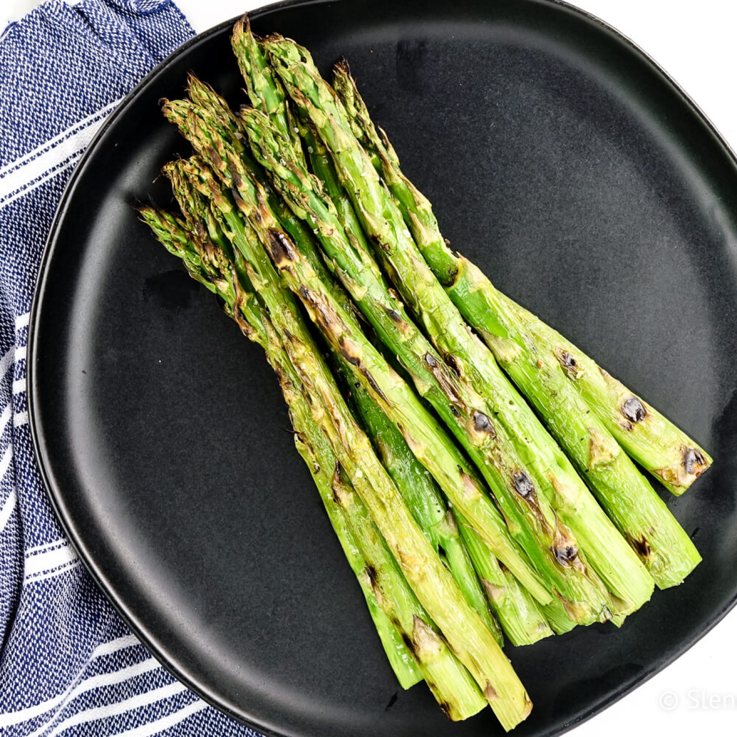 Grilled asparagus with olive oil, salt, and pepper on a black plate.