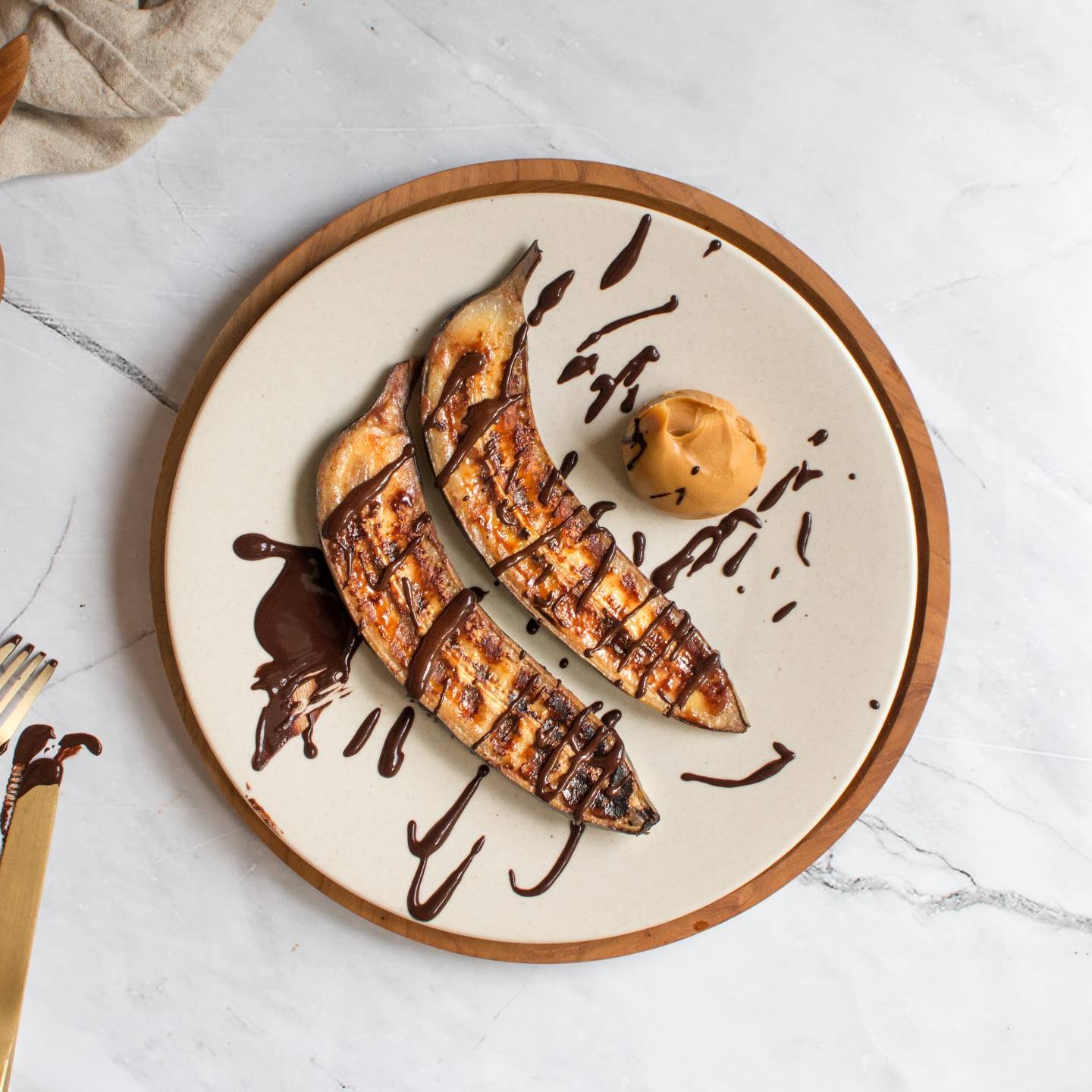 Grilled bananas on a plate with peanut butter, chocolate, and cinnamon. 