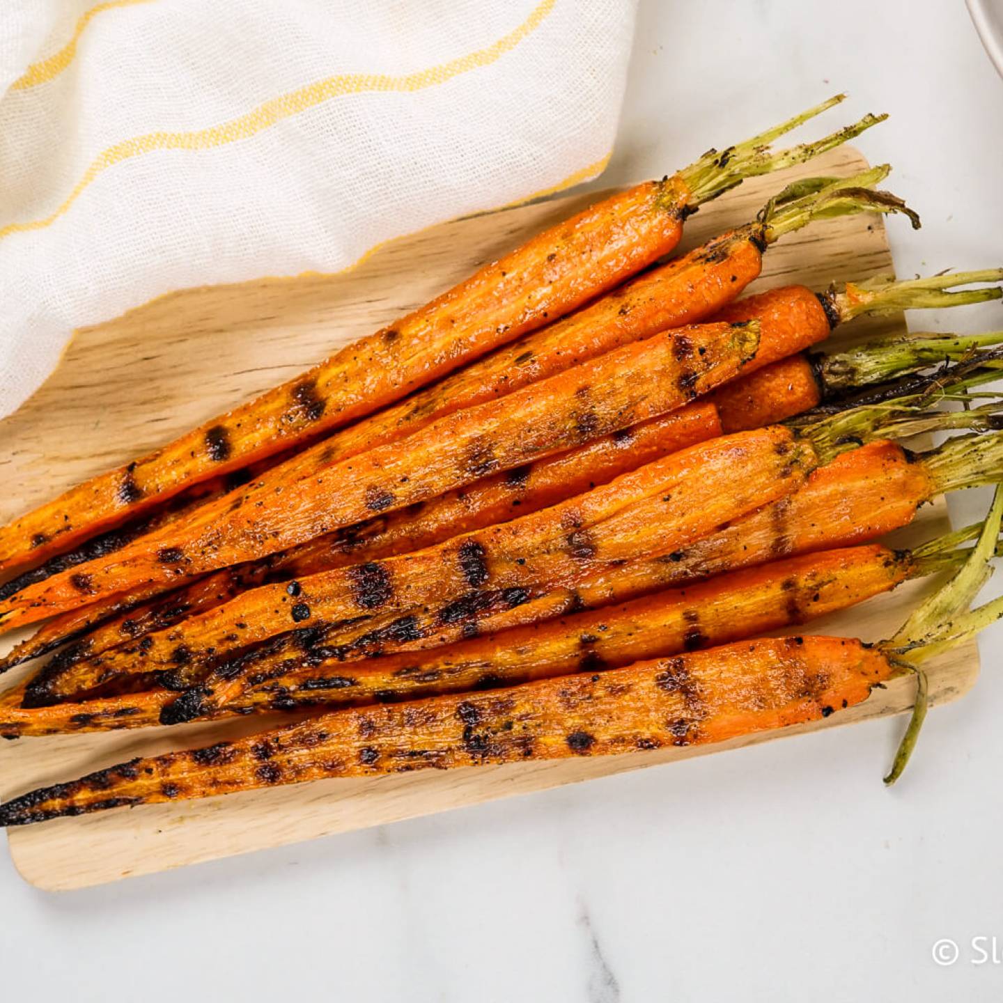 Grilled carrots with charred grill marks on a cutting board with sauce on the side.