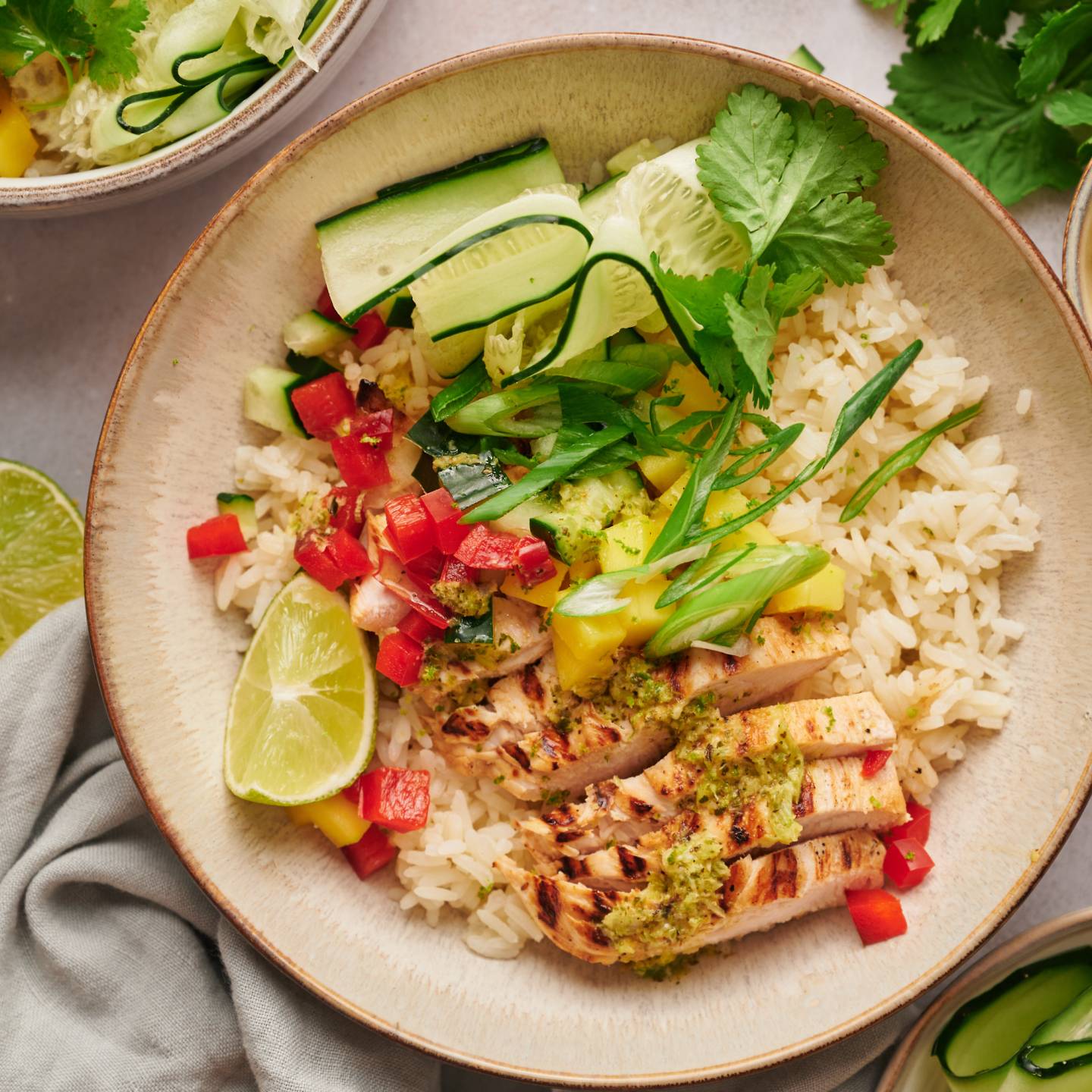 Grilled chicken bowls with citrus grilled chicken breast, rice, mango, red bell pepper, and cucumber in a bowl with cilantro.