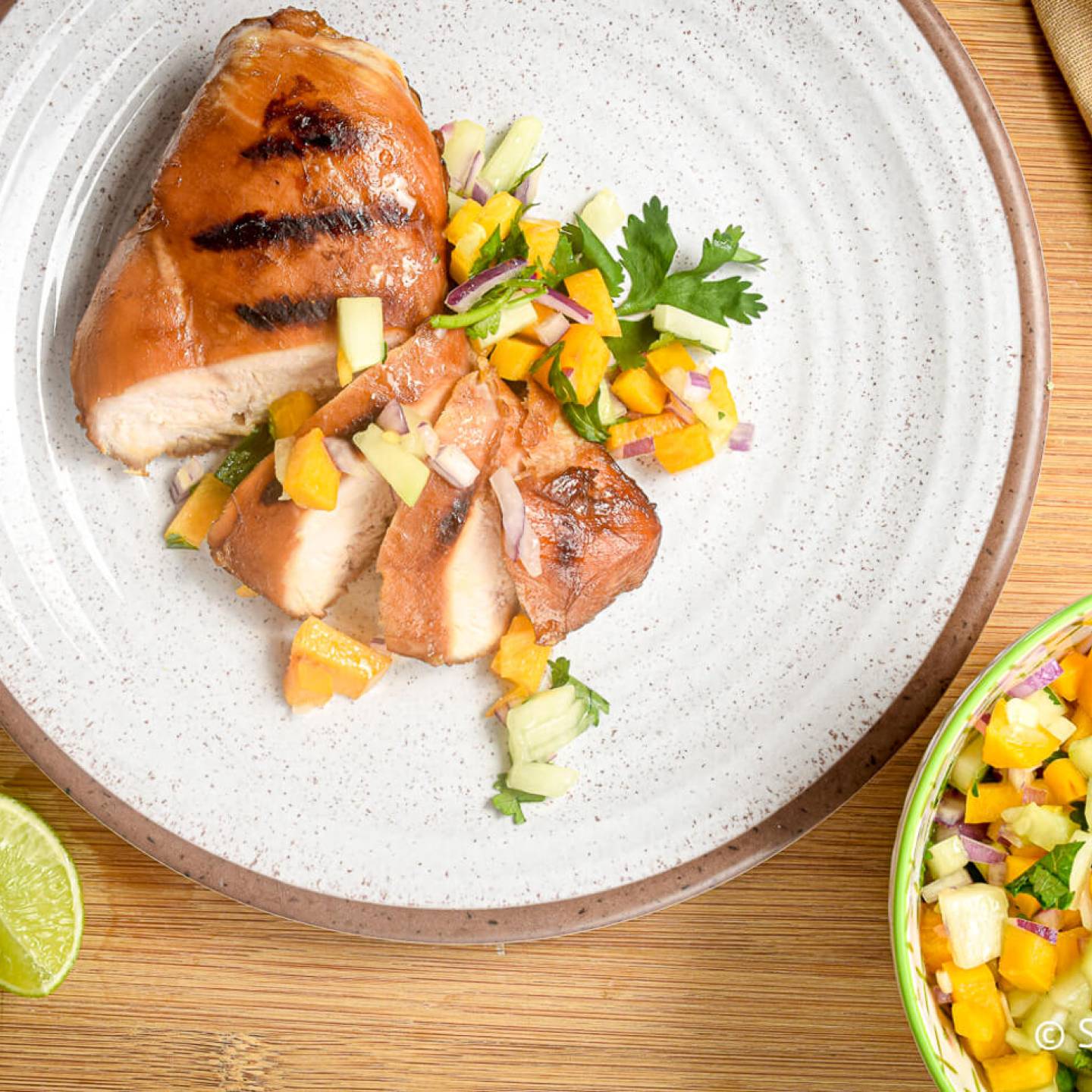 Grilled chicken with peach and cucumber salsa sliced on a plate.