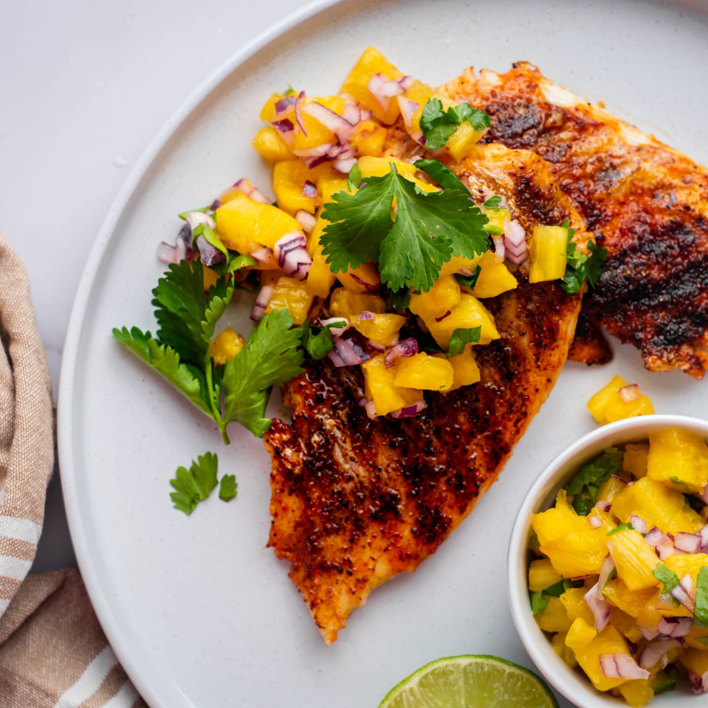 Grilled mahi mahi with paprika spice rub and pineapple salsa served on a white plate.