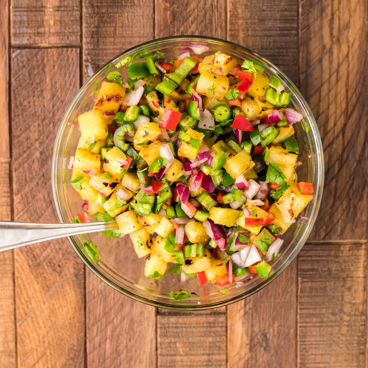 Grilled pineapple salsa served on steak tacos with chopped grilled pineapple, serrano peppers, red onion, red bell pepper, lime juice, and cilantro in a wooden bowl.