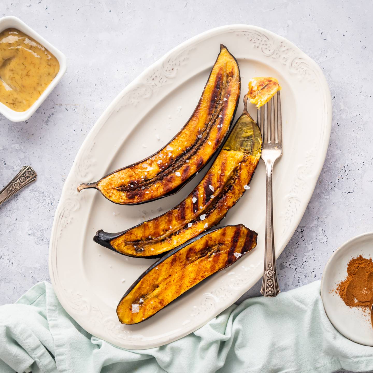 Grilled plantains with dark brown grill marks on a plate with cinnamon on the side.