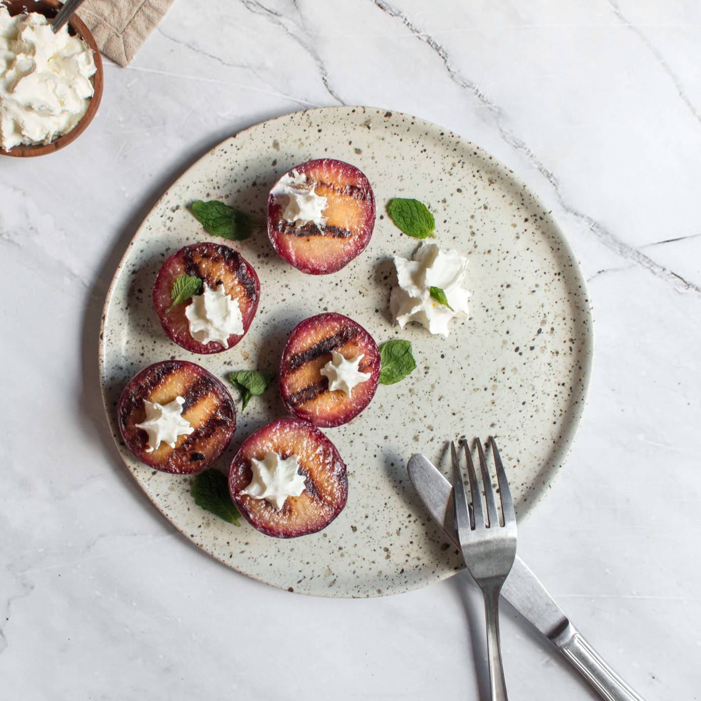 Grilled plums on a plate with honey, butter, cinnamon, and a dollop of whipped cream.