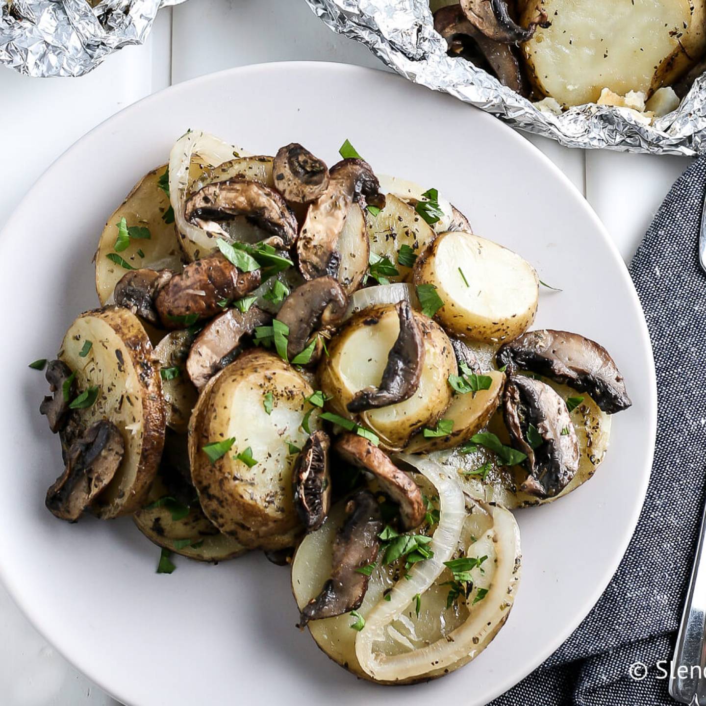 Grilled potatoes with onions, mushrooms, and butter on a plate. 