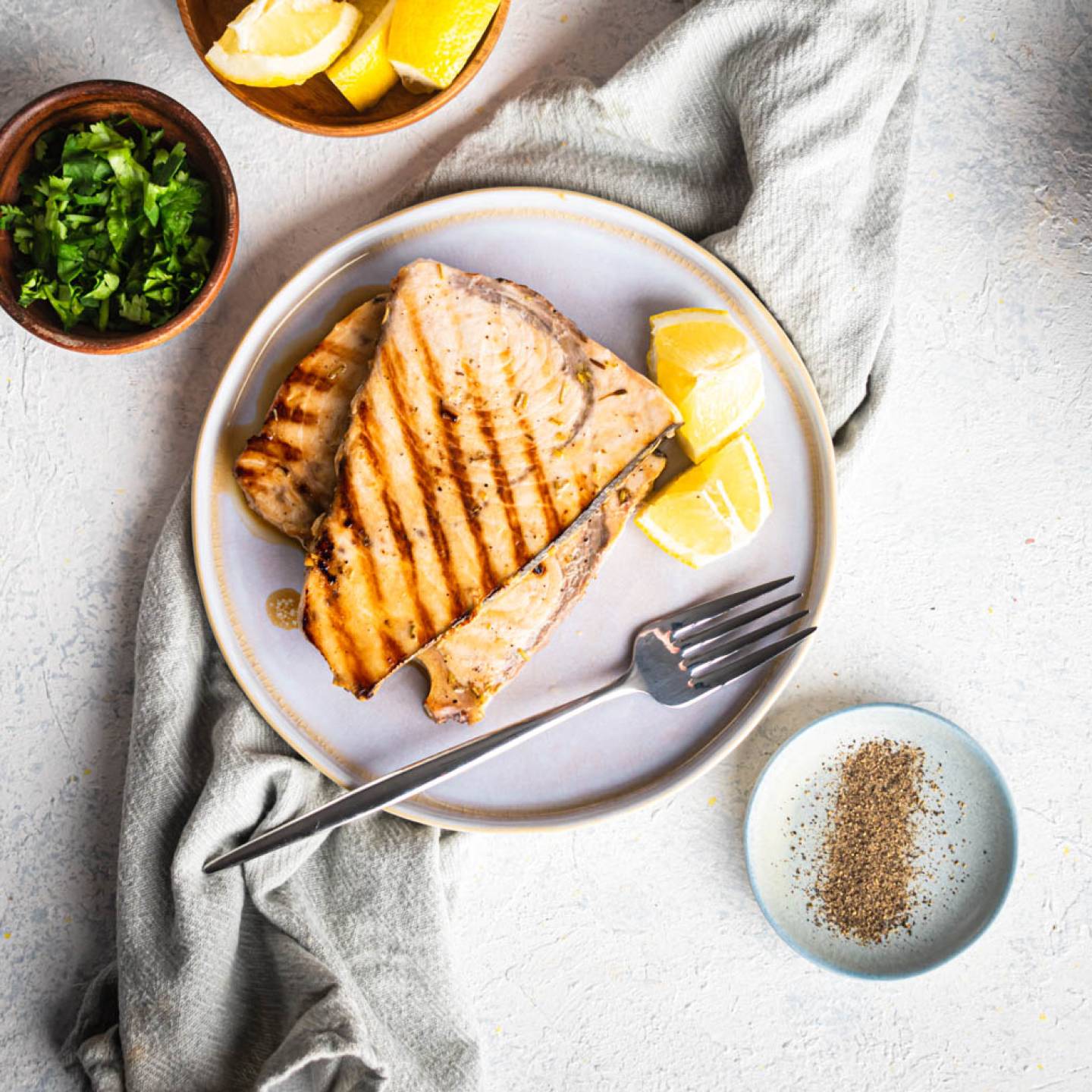 Grilled swordfish with garlic, lemon, and herbs on a plate with fresh parsley.