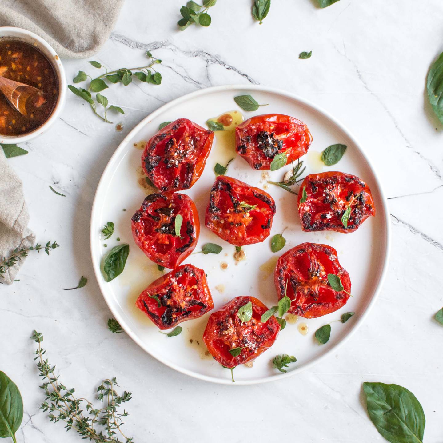 Grilled tomatoes with basil, balsamic vinegar, and garlic on a plate with fresh herbs.