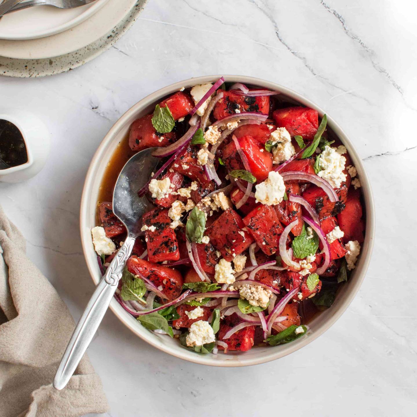 Grilled watermelon salad with feta cheese, fresh mint, basil, red onion, and balsamic vinegar in a bowl. 