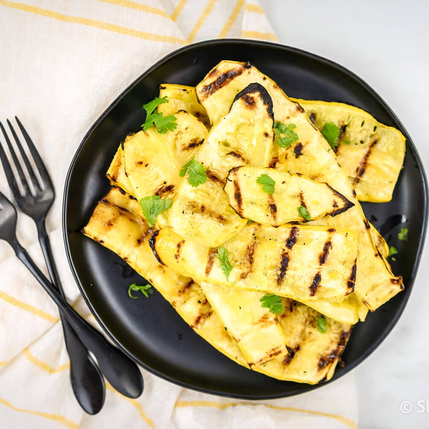 Grilled yellow squash on a black plate sprinkled with parsley.