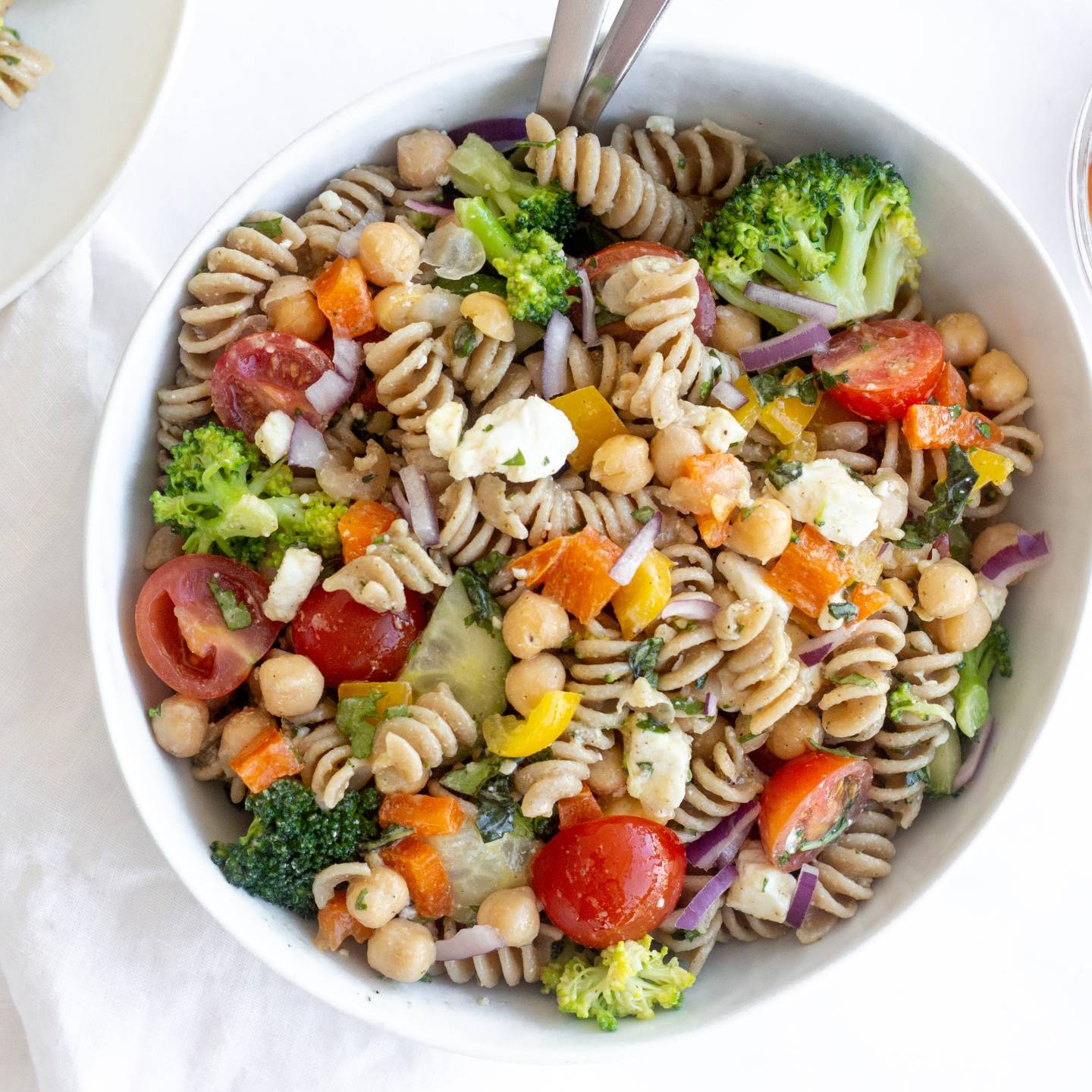 Vegetable pasta salad with cooked whole wheat pasta, chopped fresh vegetables, chickpeas, and feta cheese topped with lemon dressing.