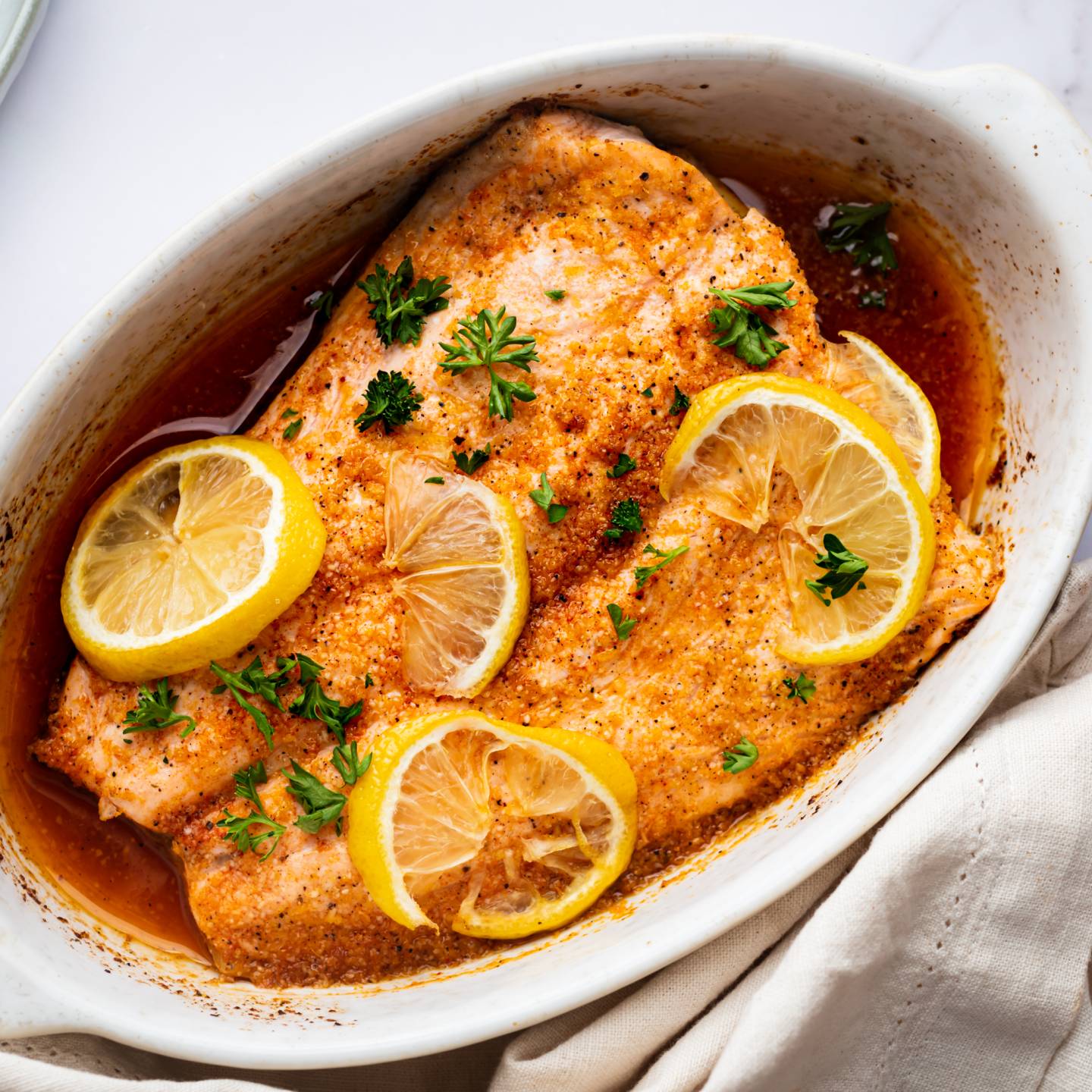 Lemon pepper salmon with slices on lemon and parsley in a white baling dish.