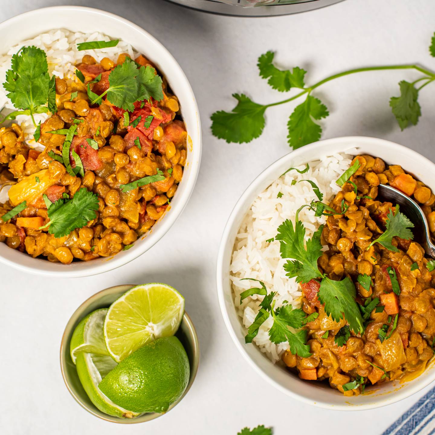 Bowls of lentil coconut curry served over white rice, garnished with fresh cilantro and lime wedges.