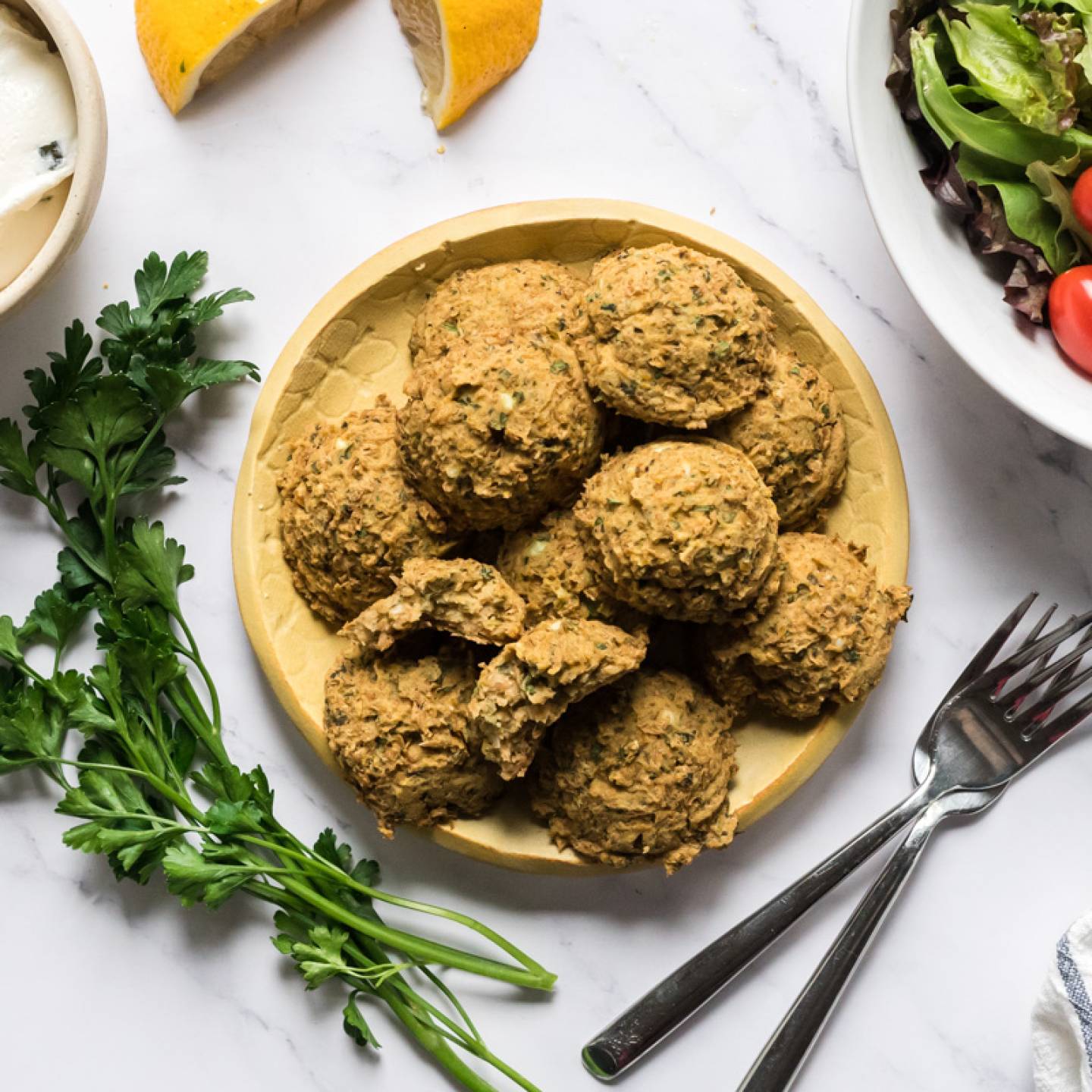 Baked lentil falafel on plate served with lemon, yogurt sauce, and salad.