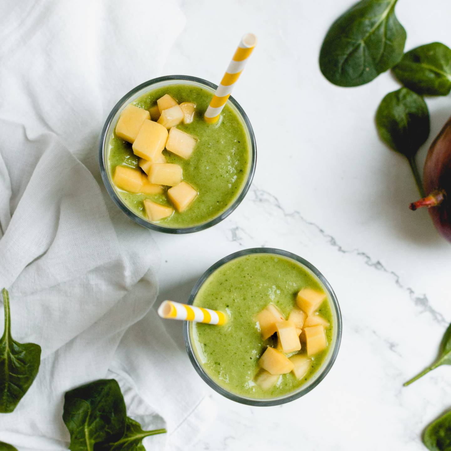 Mango spinach smoothie in two cups with fresh mango chunks on top.