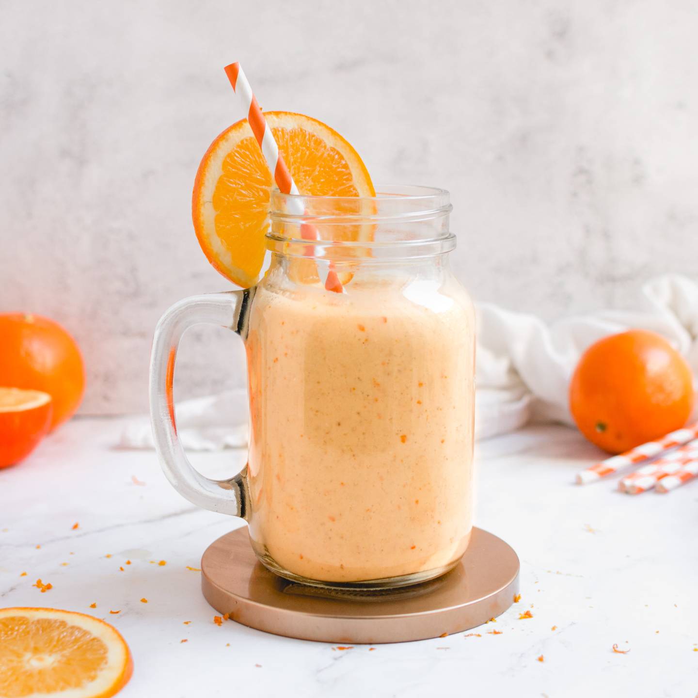 Orange creamsicle smoothie made with bananas and oranges in a glass with an orange striped straw.