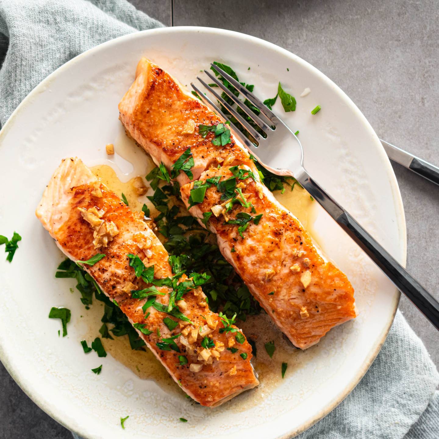 Pan seared salmon with garlic, lemon, and butter served on a plate with a lettuce and tomato salad.