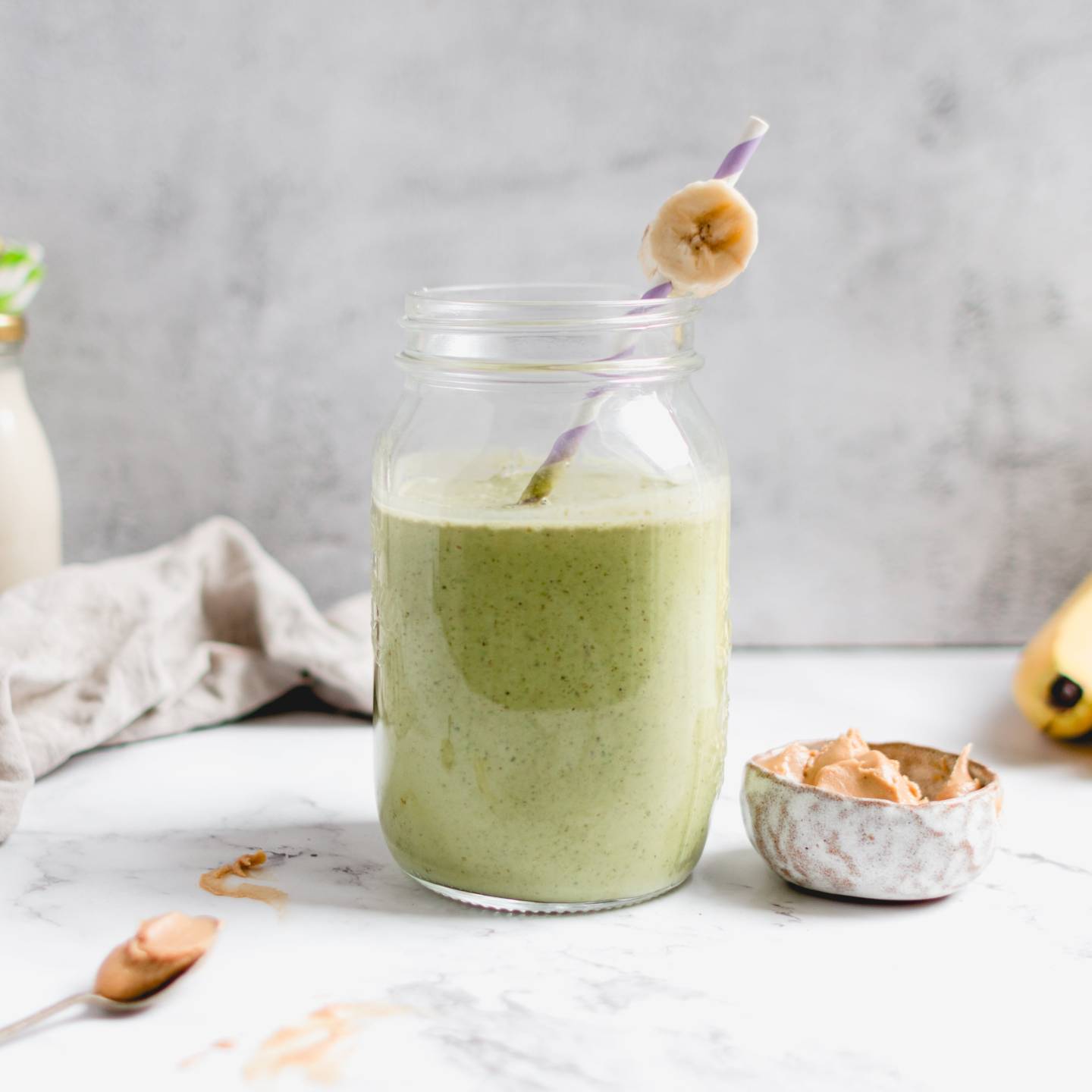 Peanut butter banana green smoothie served in a glass with a slice of banana and a straw.