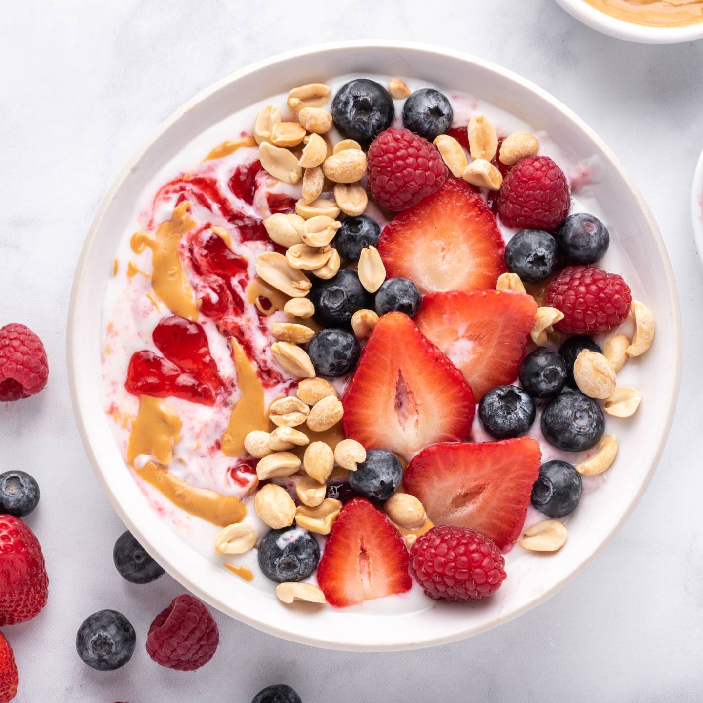Peanut butter and jelly yogurt bowl with peanut butter, strawberry jelly, peanuts, and fresh fruit.