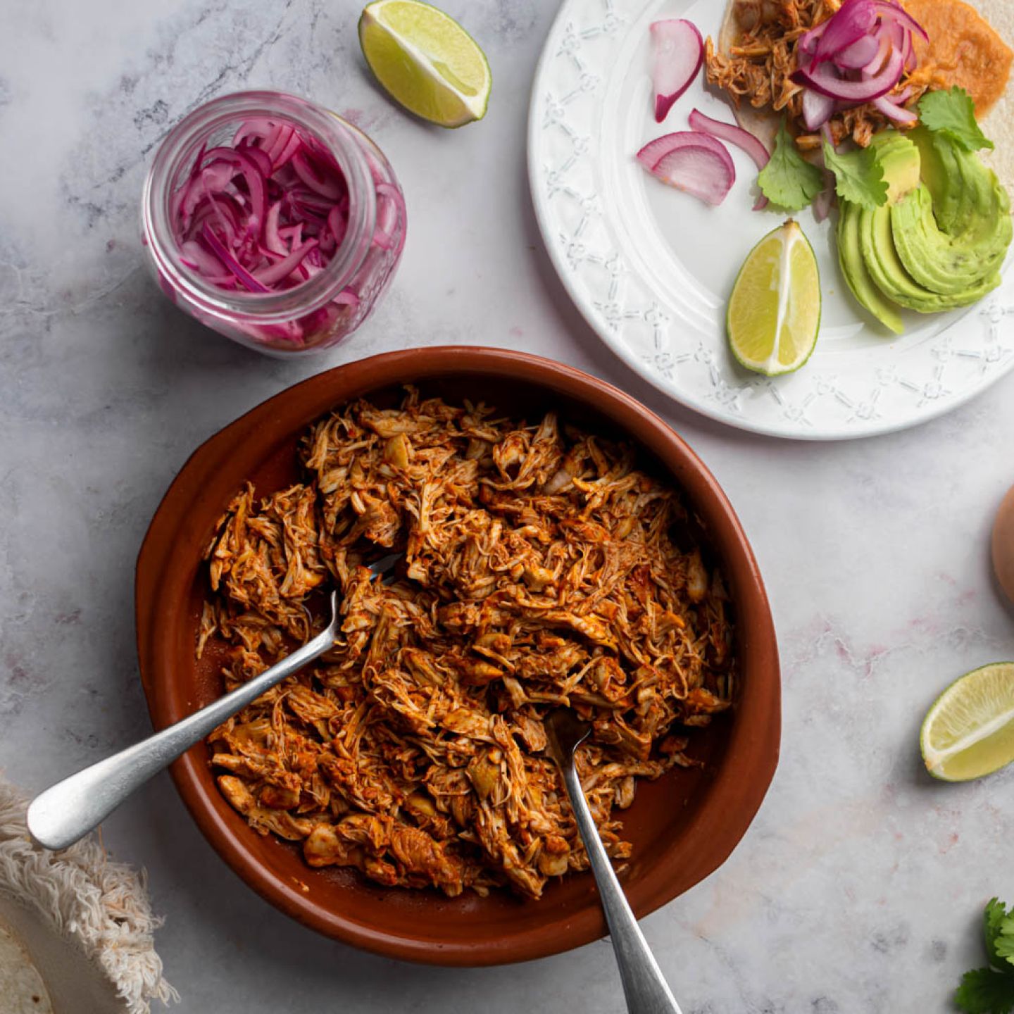Mexican pollo pibil shredded in a bowl and served in a corn tortilla with pickled onions and habanero salsa.