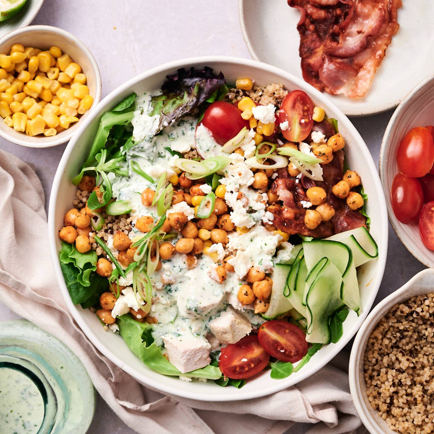Protein packed salad bowls with chicken, bacon, chickpeas, cucumbers, quinoa, cherry tomatoes, green onions, and cottage cheese dressing.