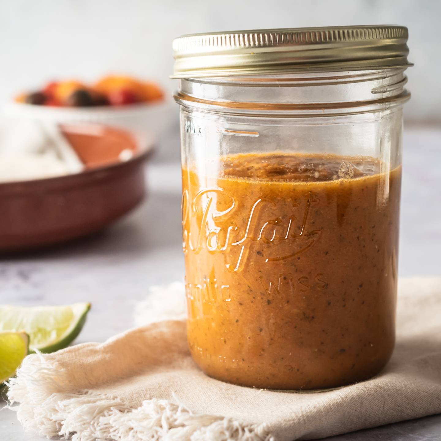 Homemade ranchero sauce in a glass jar with limes and tomatoes on the side.