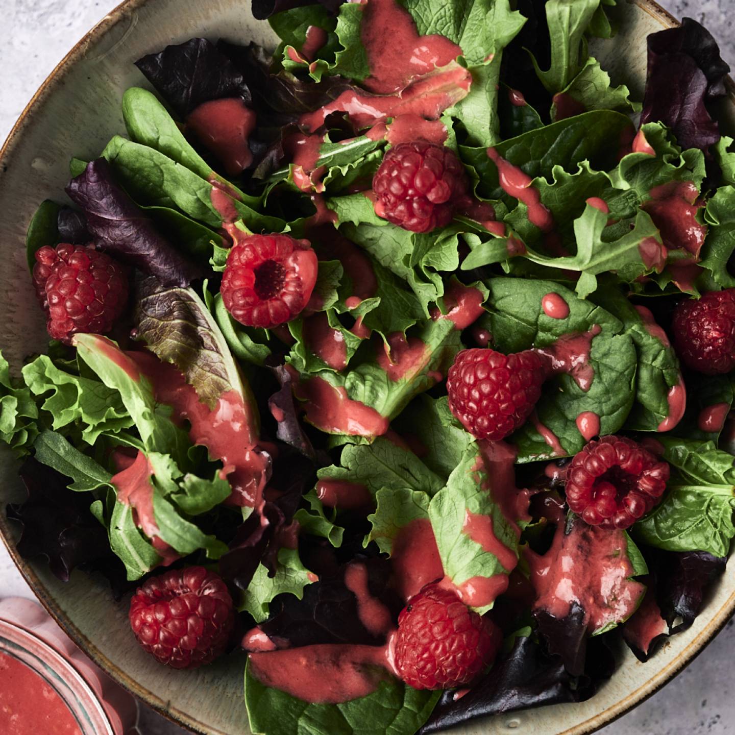 Fresh mixed greens topped with ripe raspberries and drizzled with a vibrant raspberry dressing in a decorative bowl.