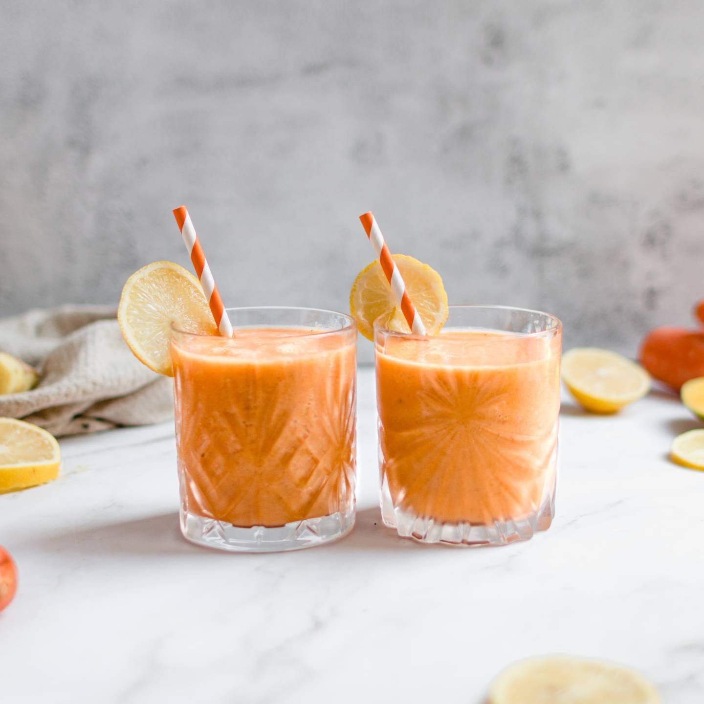 Carrot ginger smoothie with shredded carrots, banana, and mango in two glasses with straws.