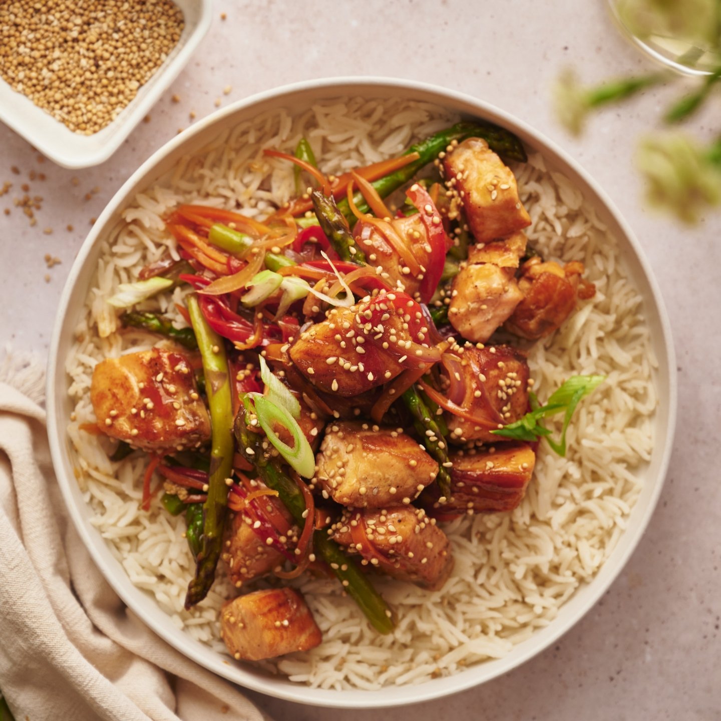 Salmon stir fry with chunks of salmon, asparagus, carrots, and red pepper in a bowl with steamed rice. 