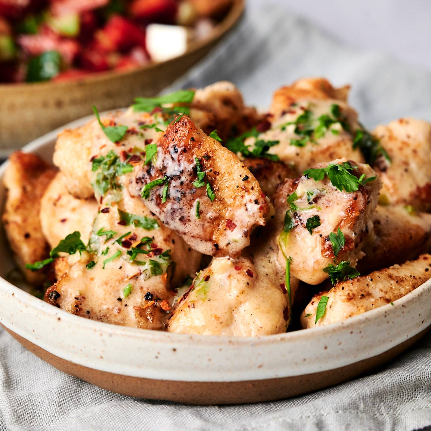 Sauteed lemon pepper chicken with creamy lemon sauce in a bowl with parsley and tomato salad on the side.