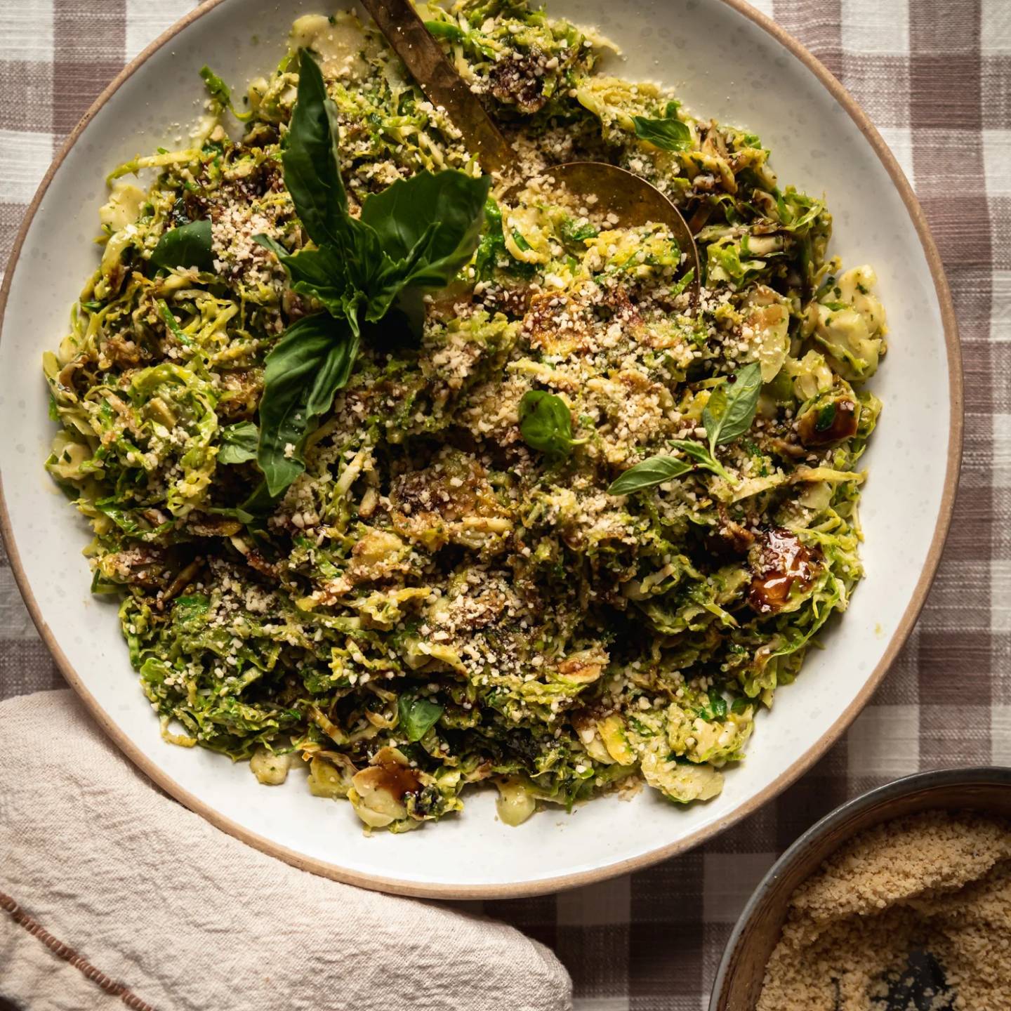 Sautéed shaved brussels sprouts with pesto in a bowl with breadcrumbs on the side.