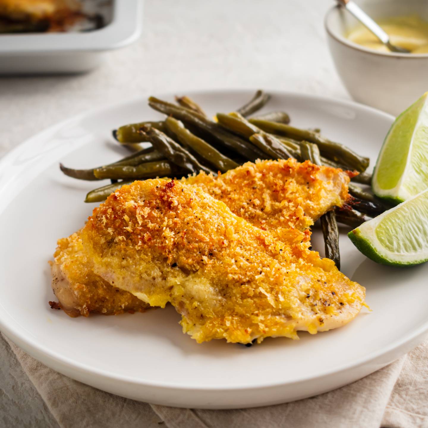 Sheet pan lemon pepper chicken coated with breadcrumbs and Parmesan cheese on a plate with roasted green beans,