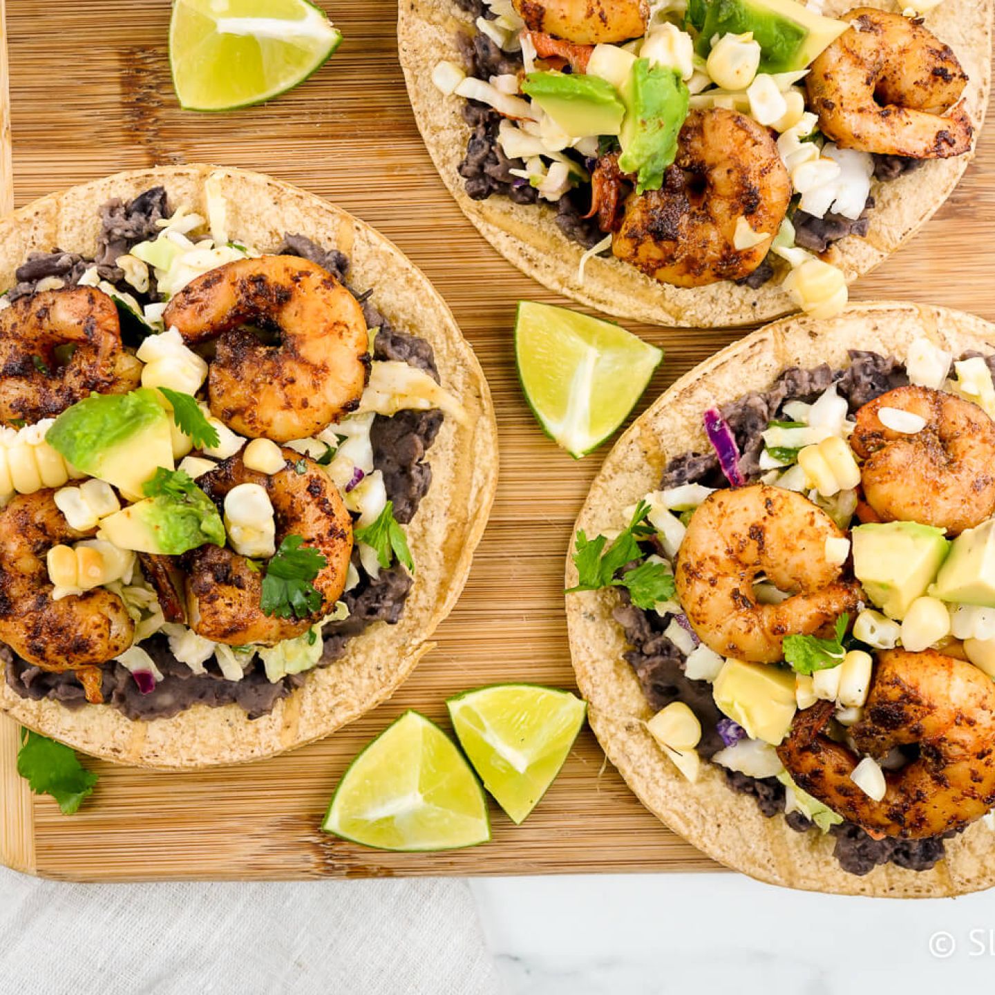 Shrimp tostadas with black beans, cabbage, spiced shrimp, avocado, and corn on baked tortillas.